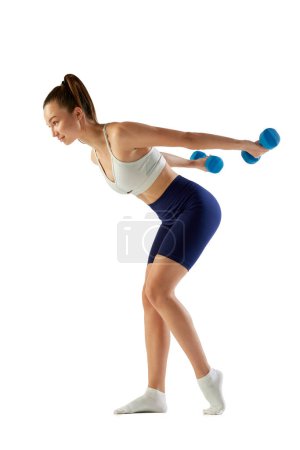 Foto de Retrato de una joven entrenadora deportiva, haciendo ejercicios con pesas aisladas sobre fondo blanco. Ejercicios de cuerpo completo. Concepto de deporte, fuerza, cuidado corporal, fitness, bienestar, salud. Anuncio - Imagen libre de derechos