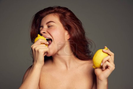 Photo for Portrait of beautiful red-haired woman, eating lemons isolated over dark grey background. Health care. Concept of beauty, natural cosmetology, hair and face treatment, cosmetics, care. Ad, poster - Royalty Free Image