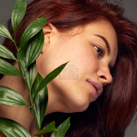 Photo for Portrait of tender red-haired woman posing with leaves isolated over dark grey background. Concept of beauty, natural cosmetology, hair and face treatment, cosmetics, care. Ad, poster - Royalty Free Image