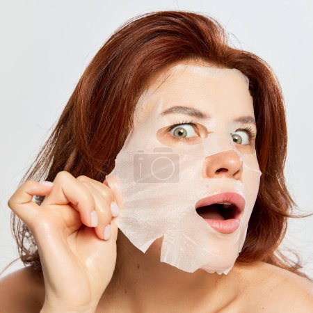 Photo for Beautiful, red-haired woman taking off moisturizing and revitalizing mask isolated on white background. Anti-wrinkles care. Concept of beauty, face and skin care, cosmetology, natural cosmetics, spa - Royalty Free Image
