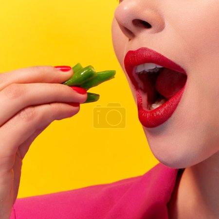 Foto de Imagen de cerca recortada de una mujer joven, boca con lápiz labial rojo comiendo judías verdes hervidas sobre fondo amarillo. Nutrición y salud. Fotografía de arte pop de comida. Colores complementarios. Copiar espacio para anuncio - Imagen libre de derechos