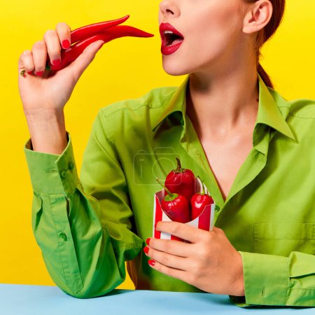Téléchargez les photos : Image recadrée de jeune femme en veste verte vintage et rouge à lèvres mangeant du piment rouge sur fond jaune. Nourriture épicée. Photographie pop art culinaire. Couleurs complémentaires. Espace de copie pour la publicité - en image libre de droit