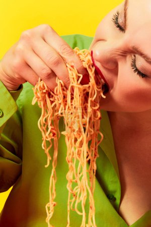 Foto de Imagen de cerca de la joven emocional comiendo espaguetis, fideos con las manos sobre el fondo amarillo. Sentir hambre, delicioso sabor. Fotografía de arte pop de comida. Colores complementarios. Copiar espacio para anuncio - Imagen libre de derechos