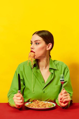 Foto de Chica joven comiendo espaguetis, fideos que salen de la boca sobre el fondo amarillo. Hora de cenar. Amante de la comida italiana. Fotografía de arte pop de comida. Colores complementarios. Copiar espacio para anuncios, texto - Imagen libre de derechos