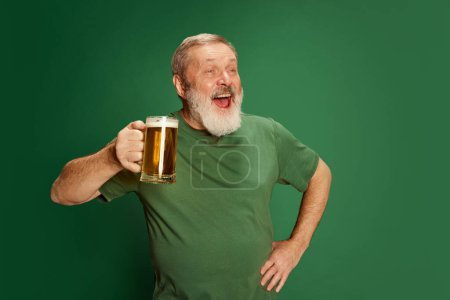 Photo for Portrait of senior man in T-shirt posing with beer isolated on green background. St Patricks Day celebration. Drunk look. Emotions, beer degustation, lifestyle, facial expression, Oktoberfest concept - Royalty Free Image