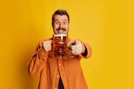 Photo for Emotive happy man in orange shirt posing with lager foamy beer glass isolated over yellow background. Sport fan. Concept of emotions, beer degustation, lifestyle, facial expression, Oktoberfest - Royalty Free Image