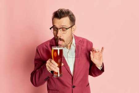 Photo for Portrait of stylish emotive man in a suit drinking, sipping lager beer isolated on pink background. Gentleman look. Concept of emotions, taste, lifestyle, facial expression, Oktoberfest - Royalty Free Image