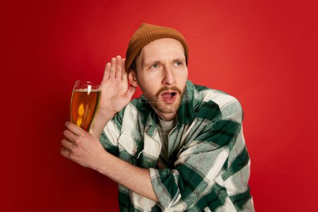 Photo for Portrait of young man in casual checkered shirt posing with beer isolated over red background. It is party time. Concept of emotions, taste, lifestyle, facial expression, Oktoberfest - Royalty Free Image