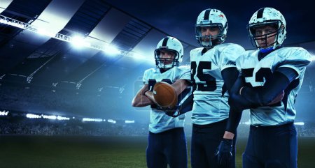 Photo for Team mates. Three american football athletes, sportsmen standing in uniform isolated at the stadium with flashlights. Concept of sport, challenges, goals, strength, competition, team. - Royalty Free Image