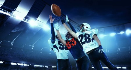Photo for In a jump. Three active american football players in motions, playing, catching ball isolated at the stadium with flashlights. Concept of sport, challenges, goals, strength, competition, team. - Royalty Free Image