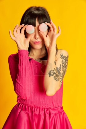 Photo for Macarons on eyes. Portrait of young beautiful girl in bright pink dress posing with dessert isolated on vivid yellow background. Concept of youth, fashion, lifestyle, emotions, facial expression. Ad - Royalty Free Image