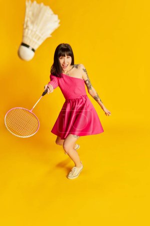 Photo for Summer hobby. Portrait of young beautiful girl in bright pink dress playing badminton isolated on vivid yellow background. Concept of youth, beauty, fashion, lifestyle, emotions, facial expression. Ad - Royalty Free Image
