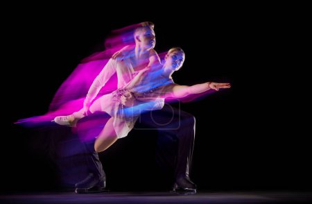 Foto de Retrato artístico de hombre y mujer, deportistas de patinaje artístico bailando aislados sobre fondo negro en neón con luces mixtas. Concepto de movimiento, deporte, belleza, hobby, competición, danza, coreografía - Imagen libre de derechos