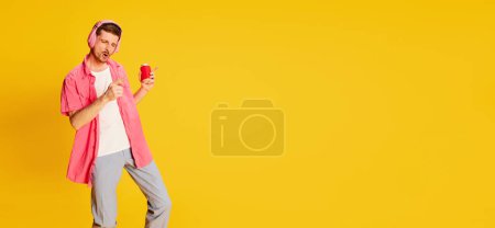 Photo for Party time.Young man in pink shirt posing in headphones isolated over vivid yellow background. Flyer. Concept of youth, lifestyle, music, fashion, emotions, facial expression. Copy space for ad - Royalty Free Image