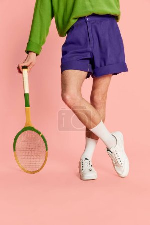 Photo for Cropped image of male legs in shorts and sneakers, leaning on tennis racket isolated over pink background. Vintage. Concept of retro fashion, sport, 90s, lifestyle, youth, emotions. facial expression - Royalty Free Image