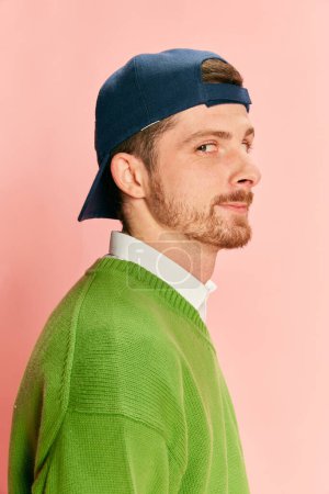 Photo for Portrait of young man in cap posing in green sweater and shirt isolated over pink background. Side view. Concept of retro fashion, sport, 90s, lifestyle, youth, emotions. facial expression. Ad - Royalty Free Image