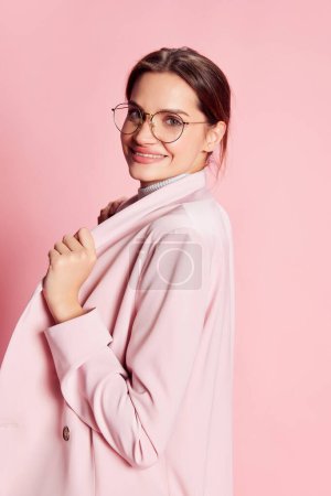 Photo for Portrait of beautiful young girl in suit and glasses posing over pink background. Cheerfully smiling. Success . Concept of youth, beauty, fashion, lifestyle, emotions, facial expression. Ad - Royalty Free Image
