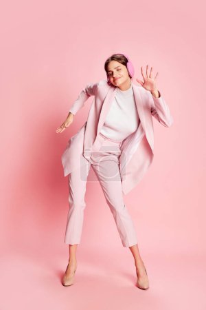 Photo for Portrait of young beautiful girl in stylish suit dancing in headphones over pink background. Positive vibe. Concept of youth, beauty, fashion, lifestyle, emotions, facial expression. Ad - Royalty Free Image