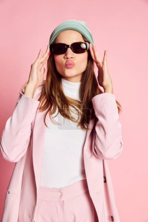 Photo for Portrait of young beautiful girl in a suit, hat and sunglasses posing over pink background. Warm, stylish clothes. Concept of youth, beauty, fashion, lifestyle, emotions, facial expression. Ad - Royalty Free Image