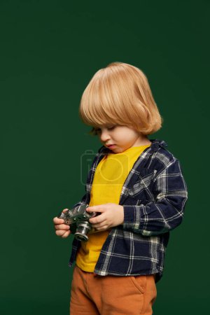 Foto de Retrato de niño pequeño, posando con cámara vintage sobre fondo de estudio verde. Fotógrafo. Concepto de infancia, emociones, estilo de vida, moda, felicidad. Copiar espacio para anuncio - Imagen libre de derechos