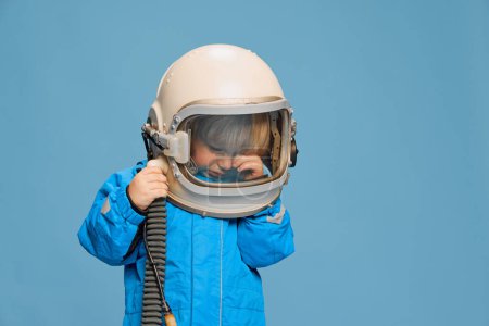 Foto de Retrato de niño pequeño, posando en traje de astronauta, llorando sobre fondo azul del estudio. Limpiando lágrimas. Concepto de infancia, emociones, estilo de vida, moda, felicidad. Copiar espacio para anuncio - Imagen libre de derechos
