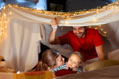 Photo for Cute family, mother, father and little daughter lying inside self-made hut, tent in room in the evening and playing. Coziness. Concept of fantasy, childhood, family, leisure time, love, care, home. - Royalty Free Image