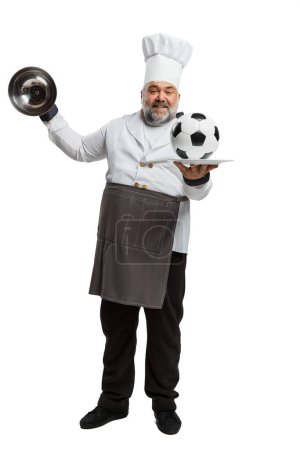 Foto de Retrato de hombre barbudo, chef de restaurante en uniforme sirviendo pelota de fútbol en plato aislado sobre fondo blanco. Coincidir. Concepto de profesión, ocupación, afición, estilo de vida, gusto. Anuncio - Imagen libre de derechos
