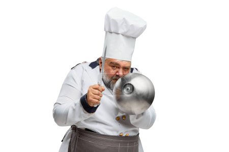 Téléchargez les photos : Portrait d'homme barbu, chef de restaurant en uniforme posant avec bol et couteau isolé sur fond blanc. Drôle de cuisinier. Concept de profession, profession, passe-temps, mode de vie, goût. Publicité - en image libre de droit