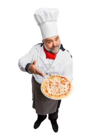 Téléchargez les photos : Portrait d'homme barbu, chef de restaurant en uniforme servant une délicieuse pizza isolée sur fond blanc. Bon dîner. Concept de profession, profession, passe-temps, mode de vie, goût. Publicité - en image libre de droit