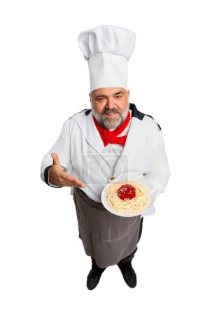 Téléchargez les photos : Portrait d'homme barbu, chef de restaurant en uniforme servant des pâtes avec sauce tomate isolée sur fond blanc. Concept de profession, profession, passe-temps, mode de vie, goût. Publicité - en image libre de droit