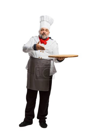 Téléchargez les photos : Portrait d'homme barbu, chef de restaurant en uniforme posant avec plateau de service isolé sur fond blanc. Une pizza. Concept de profession, profession, passe-temps, mode de vie, goût. Publicité - en image libre de droit