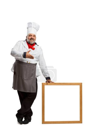 Téléchargez les photos : Portrait d'homme barbu, chef de restaurant en uniforme posant avec cadre isolé sur fond blanc. Ouverture, nouvelles, ventes. Concept de profession, profession, passe-temps, mode de vie, goût. Publicité - en image libre de droit