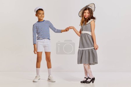 Téléchargez les photos : Portrait d'enfants, garçon en gilet rayé et adolescente en robe élégante posant sur fond gris. Mes amis. Concept d'enfance, amitié, plaisir, style de vie, mode, style rétro, émotions - en image libre de droit