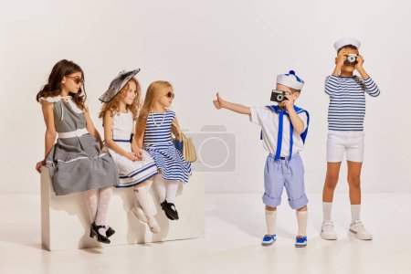 Photo for Portrait of children posing over grey background. Boys taking photo with vintage camera, girls looking. Concept of childhood, friendship, fun, lifestyle, fashion, retro style, emotions - Royalty Free Image