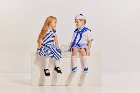 Photo for Portrait of cute little children, boy and girl in sea style clothes posing over grey background. Lovely talk. Concept of childhood, friendship, fun, lifestyle, fashion, retro style, emotions - Royalty Free Image