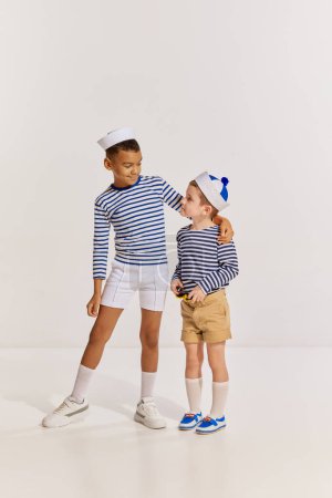 Téléchargez les photos : Portrait d'enfants, deux garçons vêtus de vêtements de style marin posant sur fond gris. De bons amis. Concept d'enfance, amitié, plaisir, style de vie, mode, style rétro, émotions - en image libre de droit