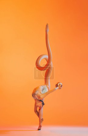 Foto de Collage de arte contemporáneo. Diseño creativo. Entrenamiento profesional de gimnasta rítmica con pelota sobre fondo naranja. Inspiración, fantasía, surrealismo, moda y estilo. Copyspace para el anuncio. Deporte. - Imagen libre de derechos