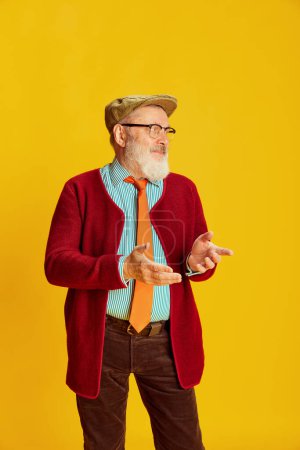 Foto de Retrato de un hombre mayor con ropa clásica, gafas y gorra posando sobre un fondo amarillo vivo. Cuestionar la cara. Concepto de emociones, expresión facial, estilo de vida, moda moderna - Imagen libre de derechos