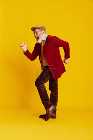 Photo for Portrait of senior man in classical clothes, glasses and cap posing over vivid yellow background. Energetic dance. Concept of emotions, facial expression, lifestyle, modern fashion - Royalty Free Image