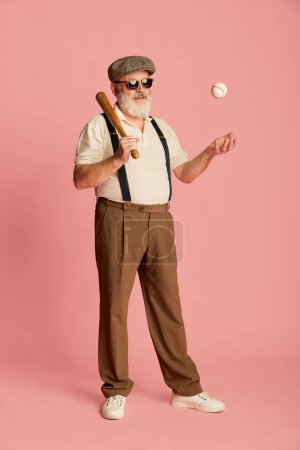 Photo for Portrait of senior man in stylish clothes with suspenders, cap and sunglasses posing with baseball bat and ball over pink background. Concept of emotions, facial expression, lifestyle, modern fashion - Royalty Free Image