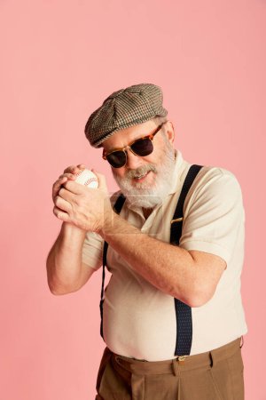 Photo for Portrait of senior man in stylish clothes, cap, suspenders and trendy sunglasses posing with baseball ball over pink background. Concept of emotions, facial expression, lifestyle, modern fashion - Royalty Free Image