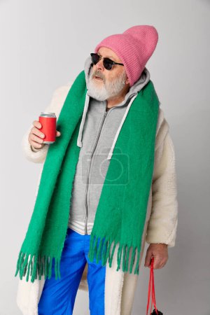 Photo for Portrait of stylish senior, old man in knitted pink hat and green scarf posing over grey background. Winter fashion look. Concept of emotions, facial expression, lifestyle, modern fashion - Royalty Free Image