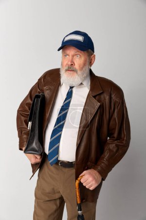 Téléchargez les photos : Portrait de vieil homme âgé en veste de cuir posant sur fond gris. Homme d'affaires, employé de bureau. Concept d'émotions, expression faciale, style de vie, mode moderne - en image libre de droit
