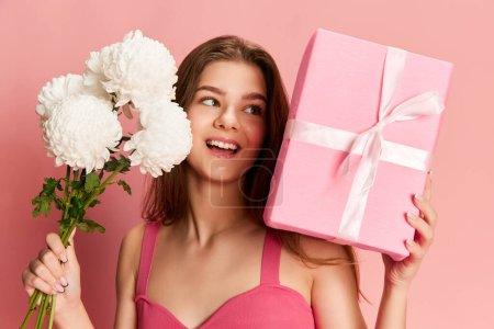 Foto de Retrato de una hermosa joven en traje lindo posando con flores blancas y caja de regalo sobre fondo rosa. Concepto de celebración, fiesta, día de la mujer, emociones, vacaciones, felicidad. Anuncio - Imagen libre de derechos
