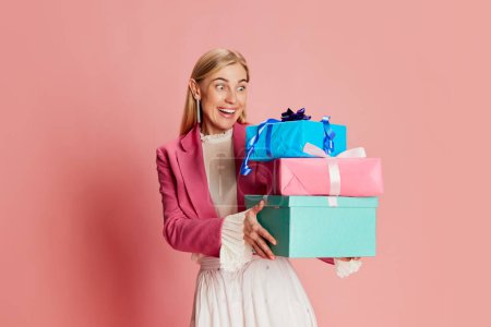Foto de Retrato de mujer hermosa y elegante posando emocionalmente con cajas presentes sobre fondo rosa. Concepto de celebración, fiesta, día de la mujer, emociones, vacaciones, cumpleaños, felicidad. Anuncio - Imagen libre de derechos