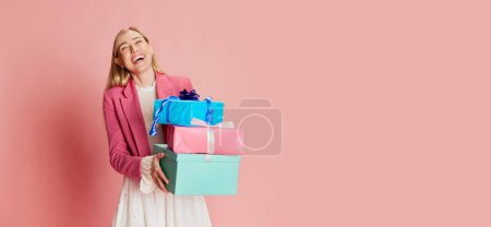 Téléchargez les photos : Souriant. Portrait de femme élégante posant émotionnellement avec des boîtes cadeaux sur fond rose. Concept de fête, fête, journée des femmes, émotions, vacances, anniversaire, bonheur. Espace de copie pour la publicité - en image libre de droit