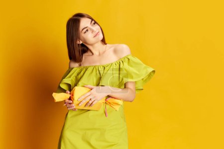 Photo for Portrait of young beautiful girl in cute dress posing over yellow background. receiving present. Concept of celebration, party, womens day, emotions, holiday, birthday, happiness. Ad - Royalty Free Image