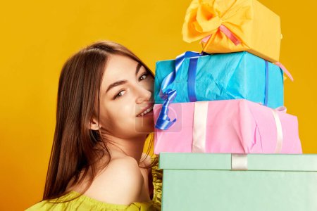 Photo for Young beautiful girl in cute dress posing with many present boxes over yellow background. Surprise, gifts. Concept of celebration, party, womens day, emotions, holiday, birthday, happiness. Ad - Royalty Free Image