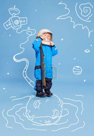 Téléchargez les photos : Design créatif avec des éléments dessinés. Portrait de petit garçon, enfant en costume d'astronaute sur fond bleu. Le futur métier. Concept d'imagination, d'enfance, de créativité, de rêves, de publicité - en image libre de droit