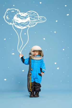 Foto de Diseño creativo con elementos dibujados. Retrato de niño, niño disfrazado de astronauta sobre fondo azul. Planeta garabatos. Concepto de imaginación, infancia, creatividad, sueños, anuncio - Imagen libre de derechos